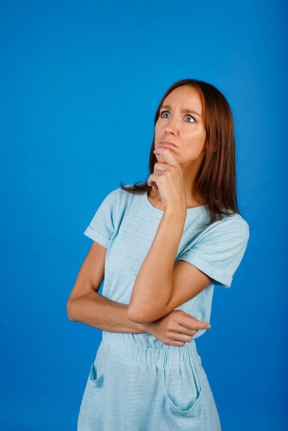 Kuva ajattelevasta nuoresta naisesta seisomassa eristyksissä sinisellä taustalla. Sivuun katsominen - Valokuva, kuva