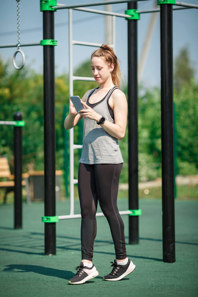 Νεαρή γυναίκα χρησιμοποιεί Smartphone στο αθλητικό πεδίο. - Φωτογραφία, εικόνα