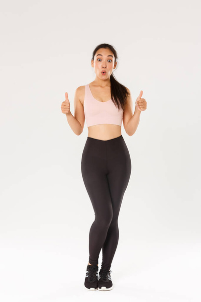 Full length of amazed and impressed female athlete in activewear, showing thumbs-up in approval and looking wondered, praise great workout program, fitness training app or gym membership prices - Photo, Image