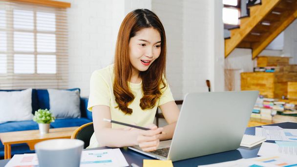 Ázsiai üzletasszony használja laptop beszélni kollégák tervről videohívás, míg okos munka otthonról a nappaliban. Önizolálás, társadalmi távolság, karantén a koronavírus megelőzésére. - Fotó, kép
