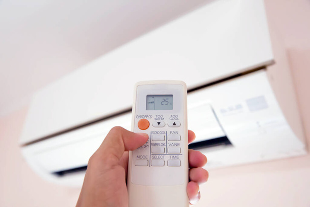 Control remoto en el primer plano de la mano, presiona el botón del interruptor de control remoto para ajustar la temperatura del aire acondicionado - Foto, imagen