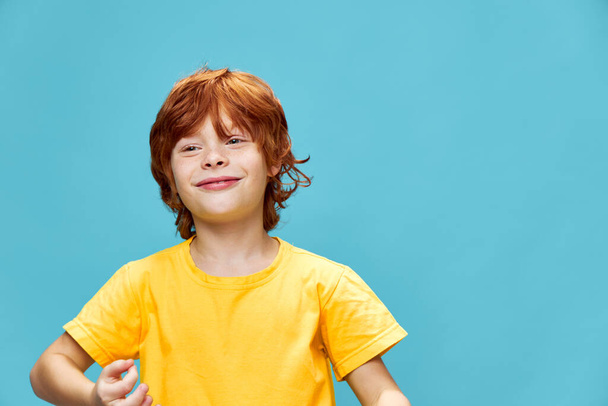  roodharig kind op een blauwe achtergrond gebaren met zijn handen - Foto, afbeelding