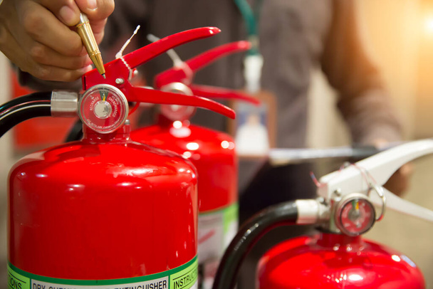 Πυροσβέστης ελέγχουν μετρητή πίεσης του κόκκινου πυροσβεστήρες δεξαμενή στο κτίριο - Φωτογραφία, εικόνα