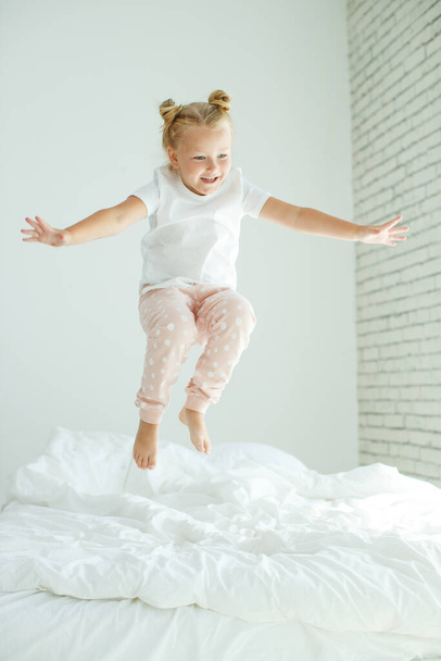 Κοριτσάκι στο κρεβάτι με λευκά λινά. Ένα παιδί στο σπίτι το πρωί ξυπνάει στο δωμάτιό του.. - Φωτογραφία, εικόνα