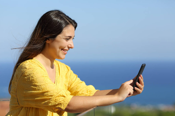 Happy woman using smart phone in a hotel balcony on the beach - Foto, Imagen