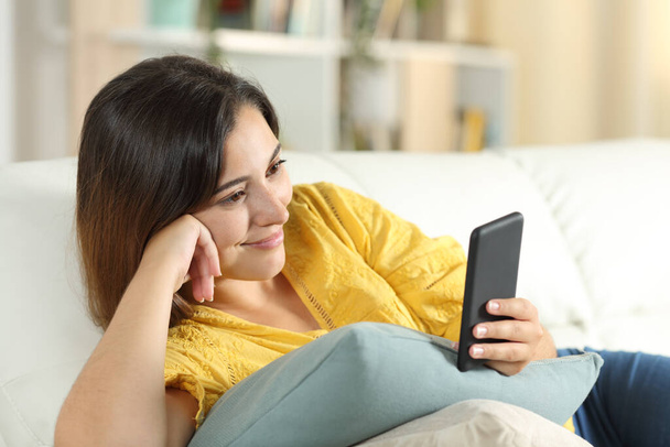 Woman watching media on smartphone lying on a sofa in the living room at home - Φωτογραφία, εικόνα