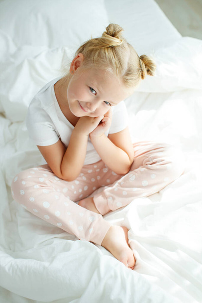 Menina na cama com linho branco. Uma criança em casa pela manhã acorda em seu quarto. - Foto, Imagem