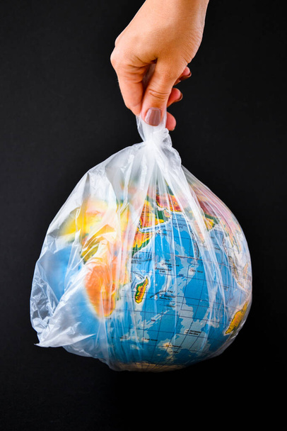 ball in the form of a globe is in a plastic bag. concept of plastic pollution of the earth. World Environment Day concept.Toy world globe in white plastic bag. Copy space for text. Save Earth - Zdjęcie, obraz