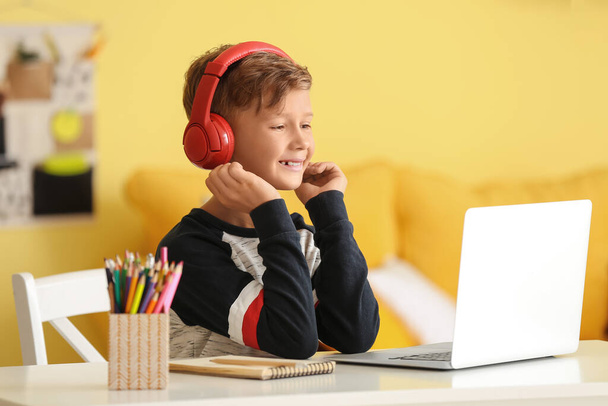 Pieni poika, jolla on kuulokkeet kannettavan tietokoneen avulla kotona - Valokuva, kuva