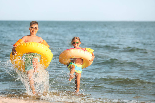 Petits enfants avec anneaux gonflables s'amusant sur la plage de la mer à la station - Photo, image