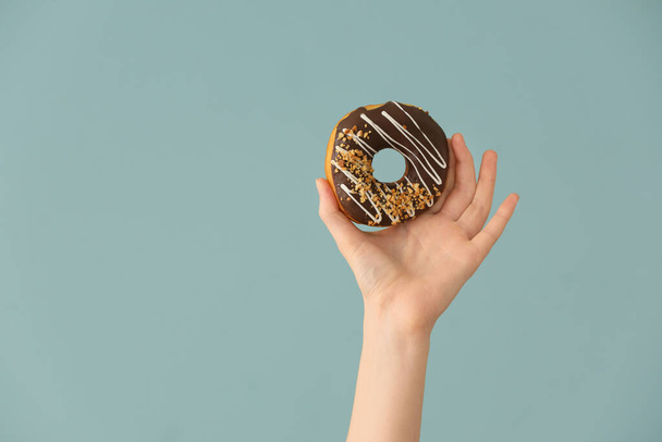 Hand with tasty donut on color background - Photo, image