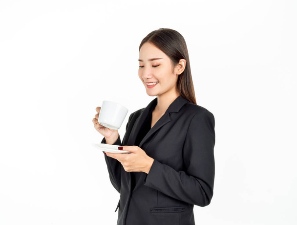 Młoda azjatycka uśmiechnięta bizneswoman w garniturze pijąca kawę na białym tle. Portret atrakcyjnej biznesmenki trzymającej biały ceramiczny kubek kawy. - Zdjęcie, obraz