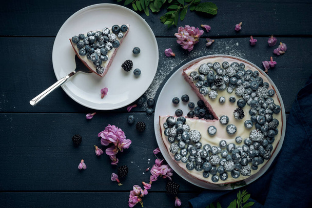 Piece of cottage cheese casserole with cake server. Cheese pie decorated with blackberry, blueberry and mint leaves on the dark wooden table. Flat lay.  - Photo, Image