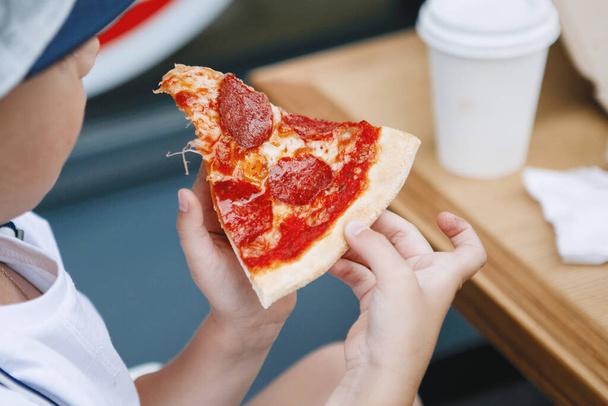 El chico tiene una rebanada de deliciosa pizza en la mano. Comida rápida, estilo italiano. - Foto, Imagen