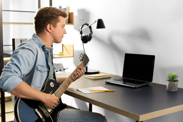 young man with laptop playing guitar at home - Fotó, kép