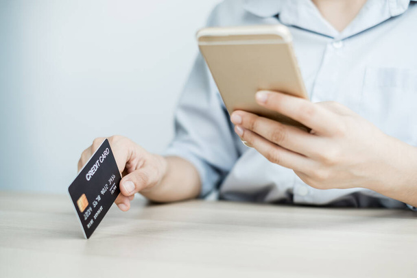 The businesswoman's hand is holding a credit card and using a smartphone for online shopping and internet payment in the office. - Photo, Image