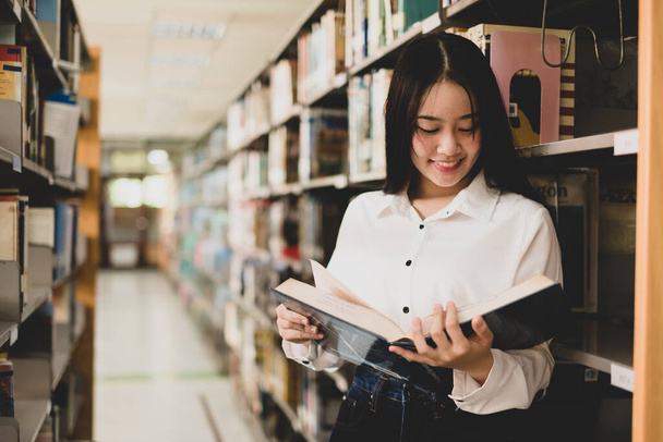 Jóvenes mujeres asiáticas están buscando libros y leyendo en las estanterías de la biblioteca de la universidad para investigar y desarrollarse en la educación. - Foto, Imagen