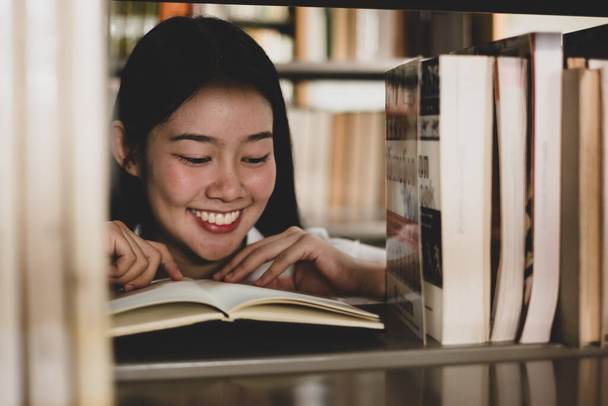 Young Asian women are searching for books and reading from the bookshelves in the college library to research and develop themselves in education. - Foto, imagen