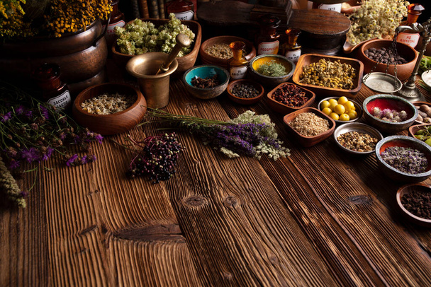 Естественная медицина. Разнообразные сухие травы в мисках и латунный раствор на деревенском деревянном столе. - Фото, изображение
