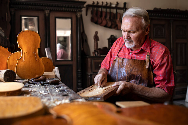 Carpintero mayor trabajando en su taller de la vieja moda. Artesano tallando madera para crear instrumento de música para violín. - Foto, Imagen