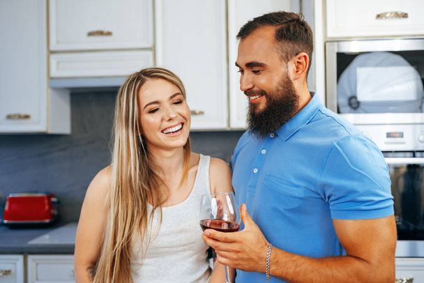 Cheerful smiling couple cooking and drinking wine in kitchen - Valokuva, kuva