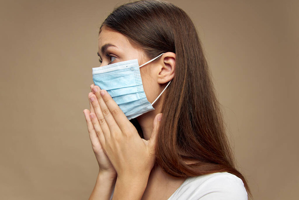 Frau mit medizinischer Maske blickt auf beigem Hintergrund zur Seite  - Foto, Bild