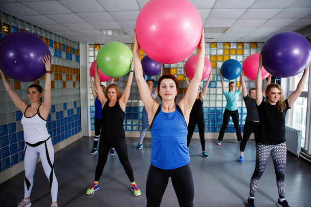 Las mujeres están sosteniendo una pelota de fitness en el gimnasio. Entrenador adulto en primer plano. Enfoque seleccionado. - Foto, Imagen