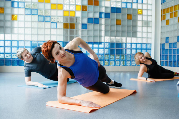 Las mujeres hacen tablón lateral en un brazo en una esterilla de yoga o fitness en el gimnasio. - Foto, Imagen