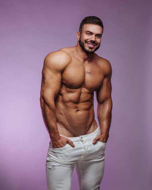 Mannelijke fitness model in witte jeans staan op roze achtergrond - Foto, afbeelding