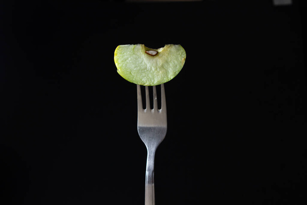 A slice of apple on a fork on a black background. Sliced green apple slice - Фото, зображення