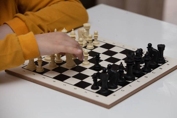 sits at a table and plays chess. The kid concentrated on the game and thinks where to make his next move. Early development, home educational games for children - Foto, immagini