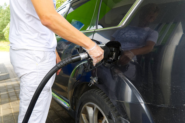 Ένας άνθρωπος ανεφοδιάζει ένα μαύρο αυτοκίνητο με καύσιμα ντίζελ σε ένα βενζινάδικο. Ακροφύσιο ανεφοδιασμού κοντά και εκτόξευση καυσίμου. - Φωτογραφία, εικόνα