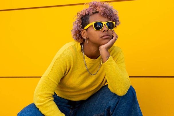 κορίτσι με κίτρινα γυαλιά ηλίου στο δρόμο εξωτερικό και κίτρινο φόντο τοίχο - Φωτογραφία, εικόνα