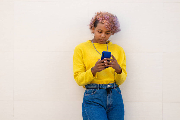 афро-американська дівчина зі смартфоном на стіні вулиці
 - Фото, зображення