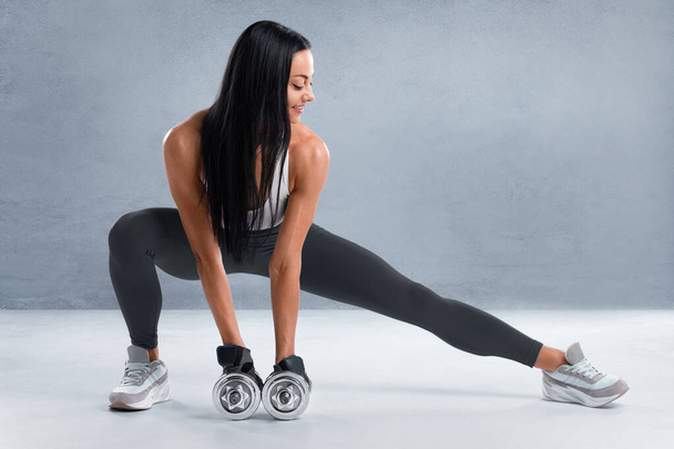 Fitness-Frau macht Ausfallübungen für Beinmuskeltraining. Aktives Mädchen, das vor dem grauen Hintergrund eine Schritt-Ausfallübung mit einem Bein macht - Foto, Bild