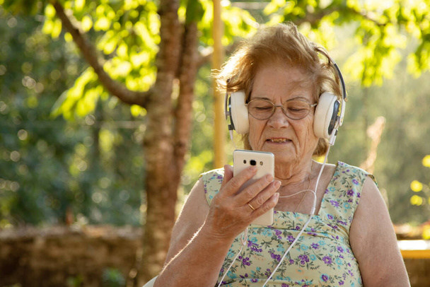 starsza kobieta z telefonem komórkowym i słuchawkami na zewnątrz - Zdjęcie, obraz