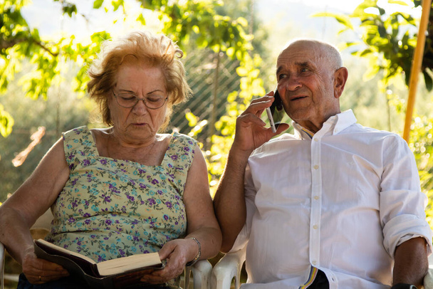 idős pár olvas egy könyvet, és beszél a mobiltelefonon - Fotó, kép