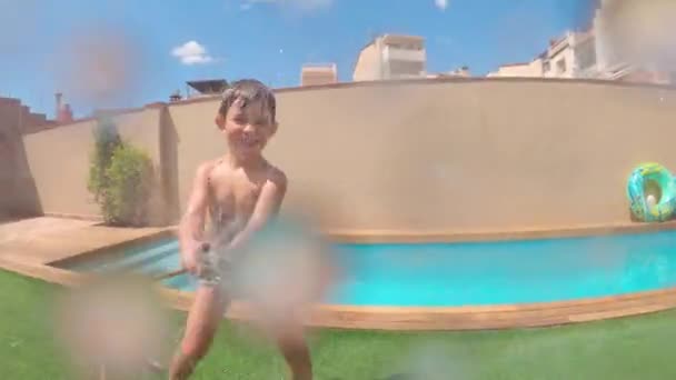 Boldog ötéves fiú játszik, hogy nedves a kamera, amely rögzíti őt. Szórakozni egy napsütéses napon. - Felvétel, videó