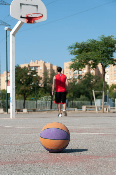 A vertical selective focus shot of a basketball in a court with the male player walking near the ring - Photo, Image