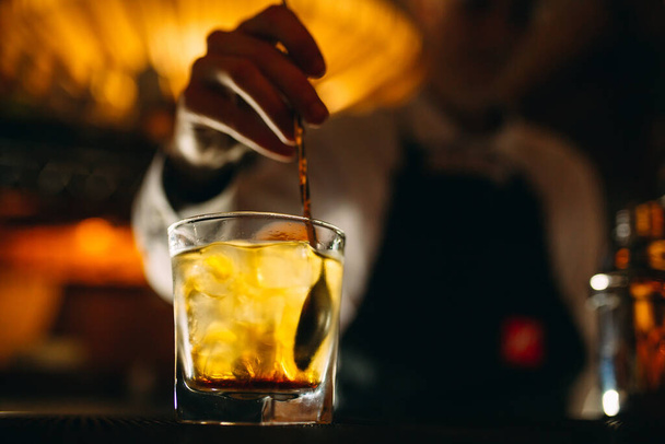 The bartender stirs a spoonful of whiskey with ice in a glass. - Photo, Image