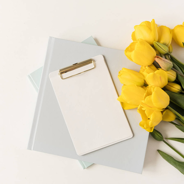 Hermoso espacio de trabajo moderno de oficina con portapapeles y papelería y flores de tulipán. Flatlay, mesa de trabajo minimalista vista superior. Hoja de papel en blanco con espacio de copia maqueta - Foto, imagen