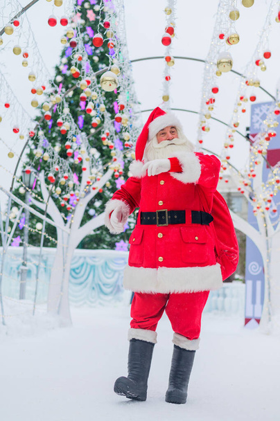 Portrait of an elderly man dressed as santa claus on the background of a christmas tree outdoors. - Foto, Bild
