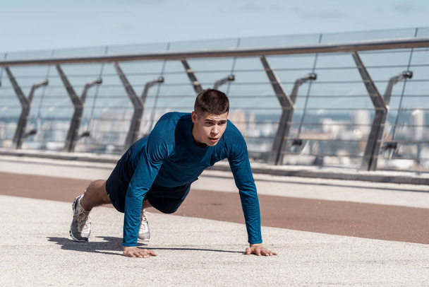 Fitness and healthy lifestyle concept. Focused young adult guy doing exercise, push ups and standing in plank pose, making sport training outdoors alone - Photo, Image