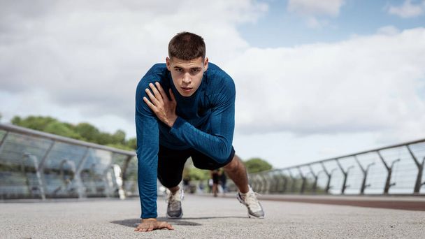 Workout and healthy lifestyle concept. Panoramic view of young athletic man doing shoulder tap exercise, push up, standing in plank pose. Sportsman looking at camera, making sport training outdoors - Fotoğraf, Görsel