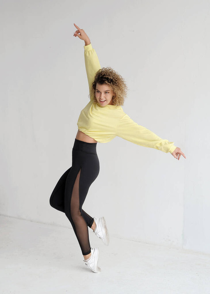 Αρκετά σγουρά μαλλιά νεαρή γυναίκα χορεύει στο στούντιο με φόντο το φως.  - Φωτογραφία, εικόνα