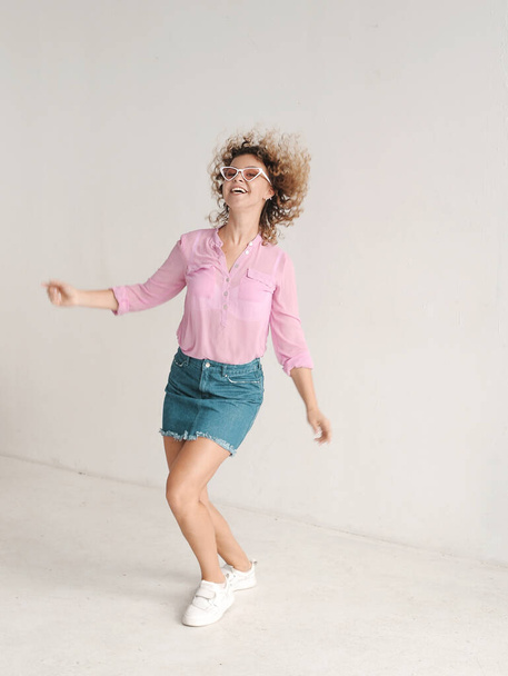 Pretty curly hair young woman dancing in studio on light background.  - Foto, Imagen