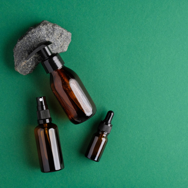Amber glass cosmetic bottles and stone on green background. Flat lay, top view. Bio nature cosmetics skin care concept - Fotografie, Obrázek