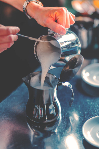 A grayscale shot of a female barista at work preparing milk for espresso coffee macchiato or cappuccino in a bar - Foto, immagini