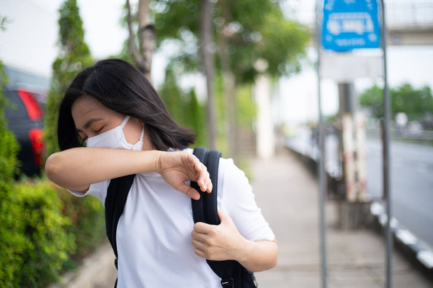 Azjatka nosząca ochronną maskę przeciw wirusowi i zanieczyszczeniu twarzy, kaszel i stojąca na przystanku autobusowym. Nowy styl życia z COVID-19 wirusa korony. - Zdjęcie, obraz