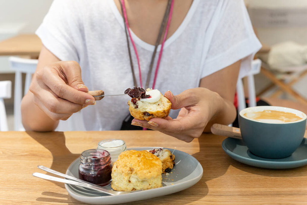Woman spreading jam on clotted scones with coffee on table - Foto, Imagem